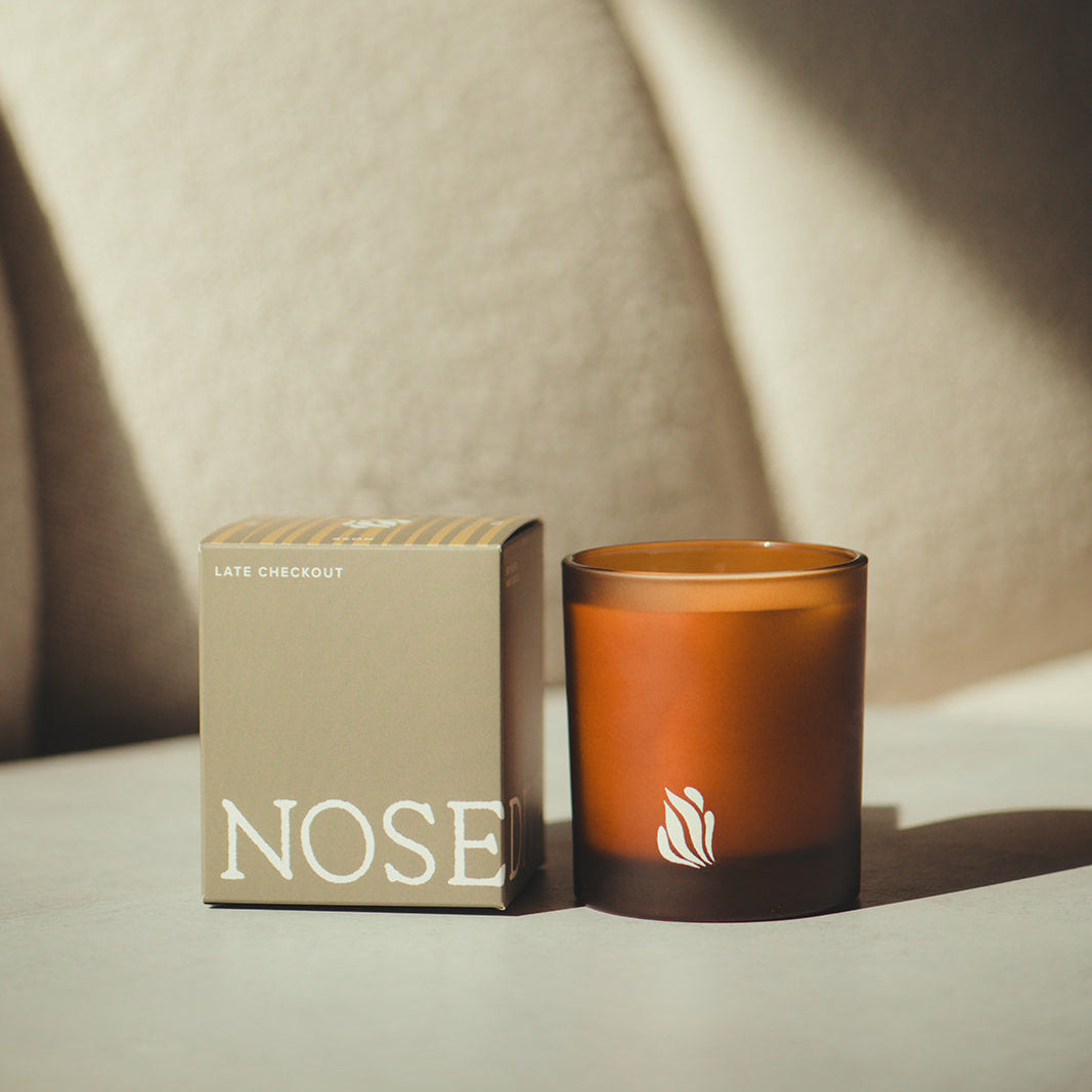 Candle and its packaging labeled 'NOSE' on a light surface with a neutral background