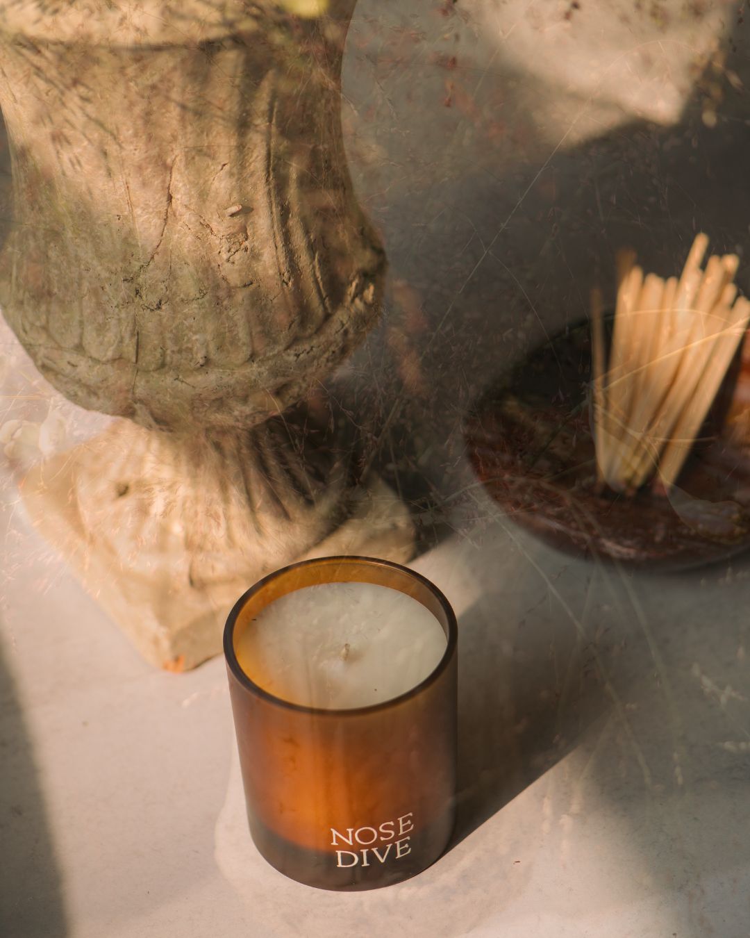 Candle labeled 'Nose Dive' on a surface with a textured background